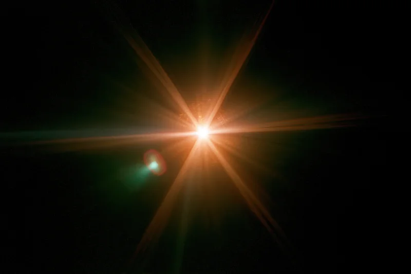 Bright point light source glowing with starburst flare against pure black background