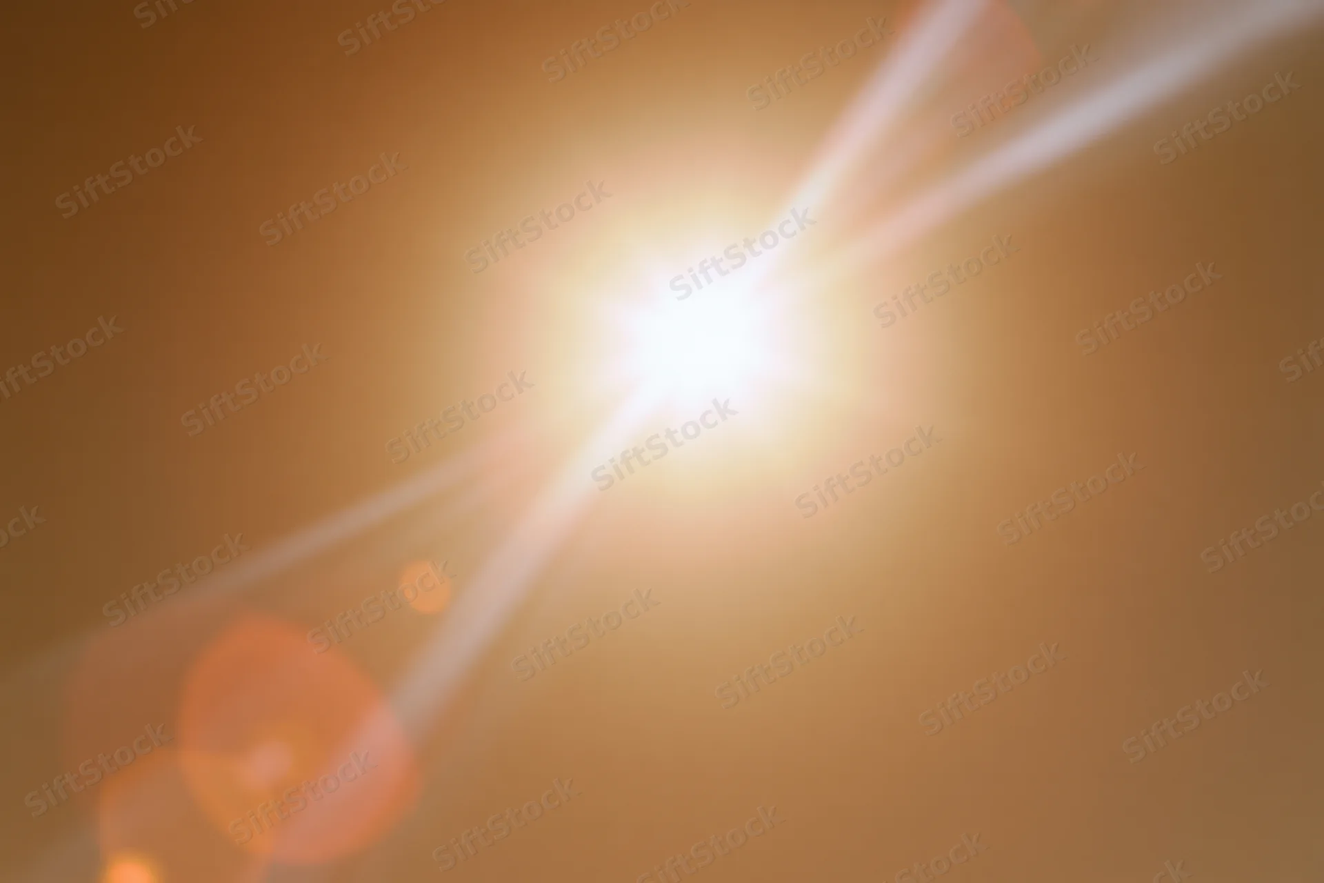 Bright sun blazing in hazy sky with lens flare and bokeh highlights