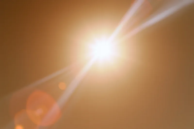 Bright sun blazing in hazy sky with lens flare and bokeh highlights