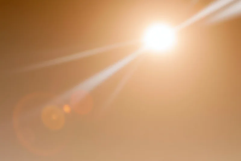 Bright sun shining in hazy sky with lens flare and warm light diffusion