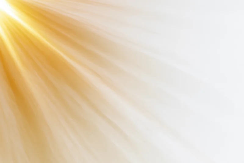 Bright golden sunlight rays bursting from the upper-left corner across a white background