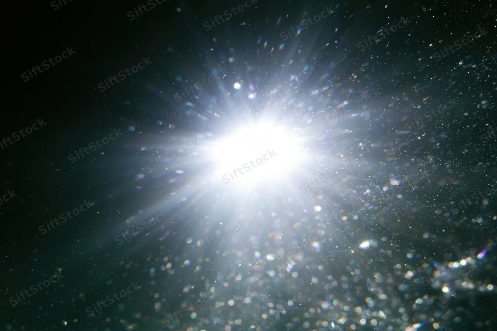 Bright white light bursting through water or glass with scattered particles and lens flare