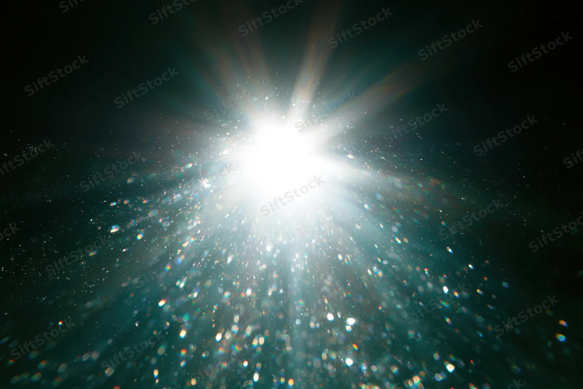 Bright white light bursting underwater with sparkling particles and lens flare