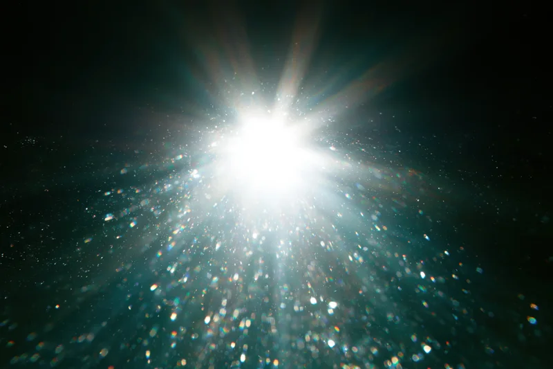 Bright white light bursting underwater with sparkling particles and lens flare