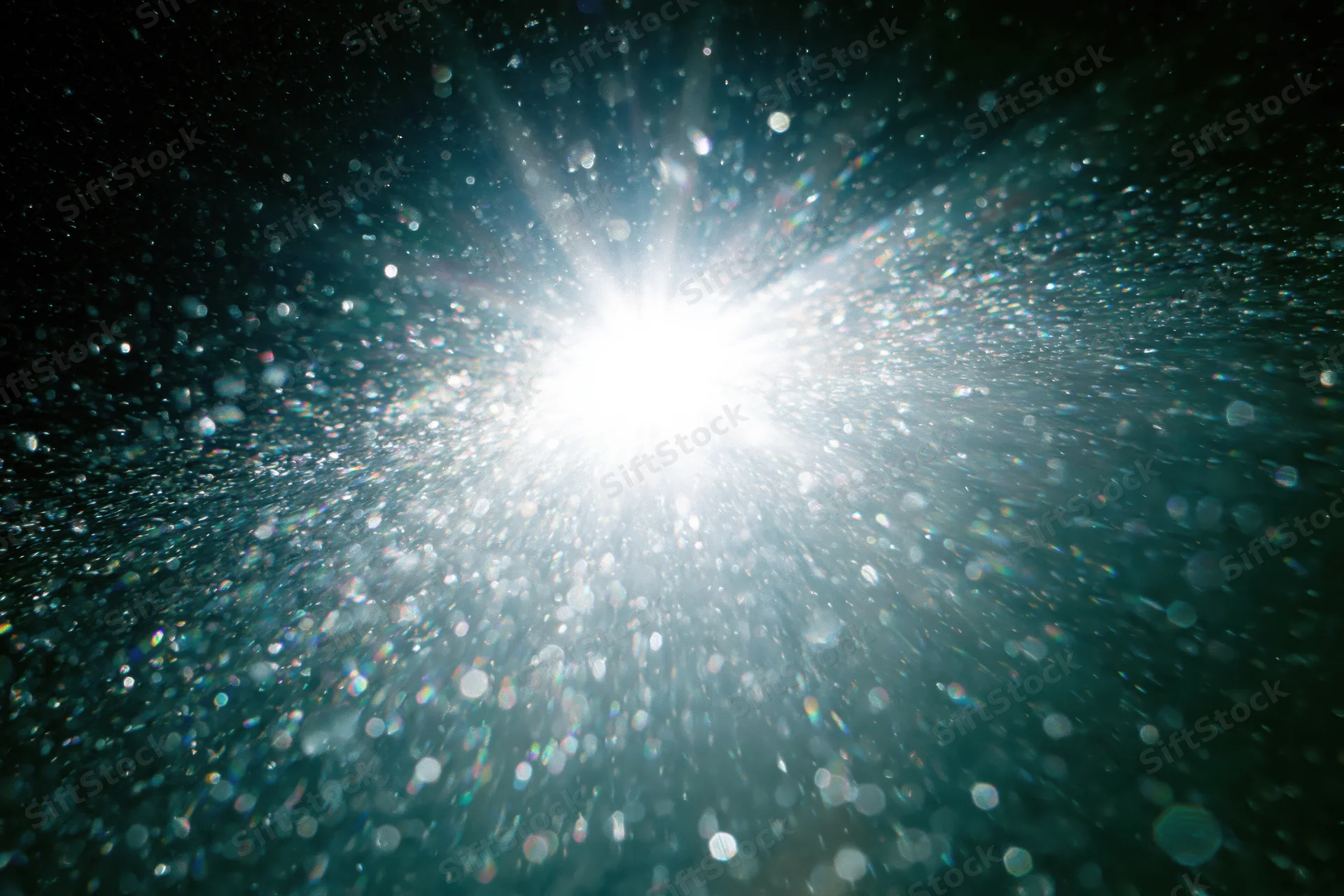 Bright white light bursting underwater with sparkling particles and lens flare