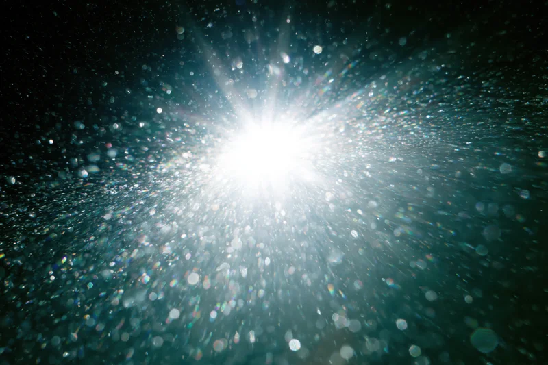 Bright white light bursting underwater with sparkling particles and lens flare