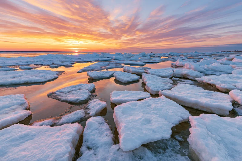 Broken ice floes scattered across a shallow frozen shoreline at sunset