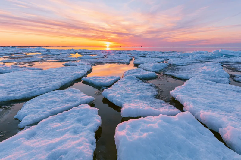Broken ice floes scattered across a shallow frozen shoreline at sunset