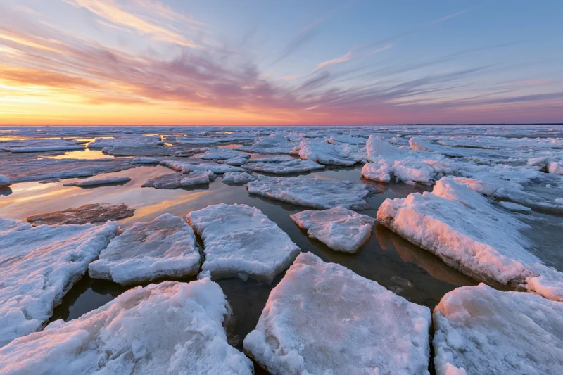 Broken ice floes scattered across a shallow frozen shoreline at sunset