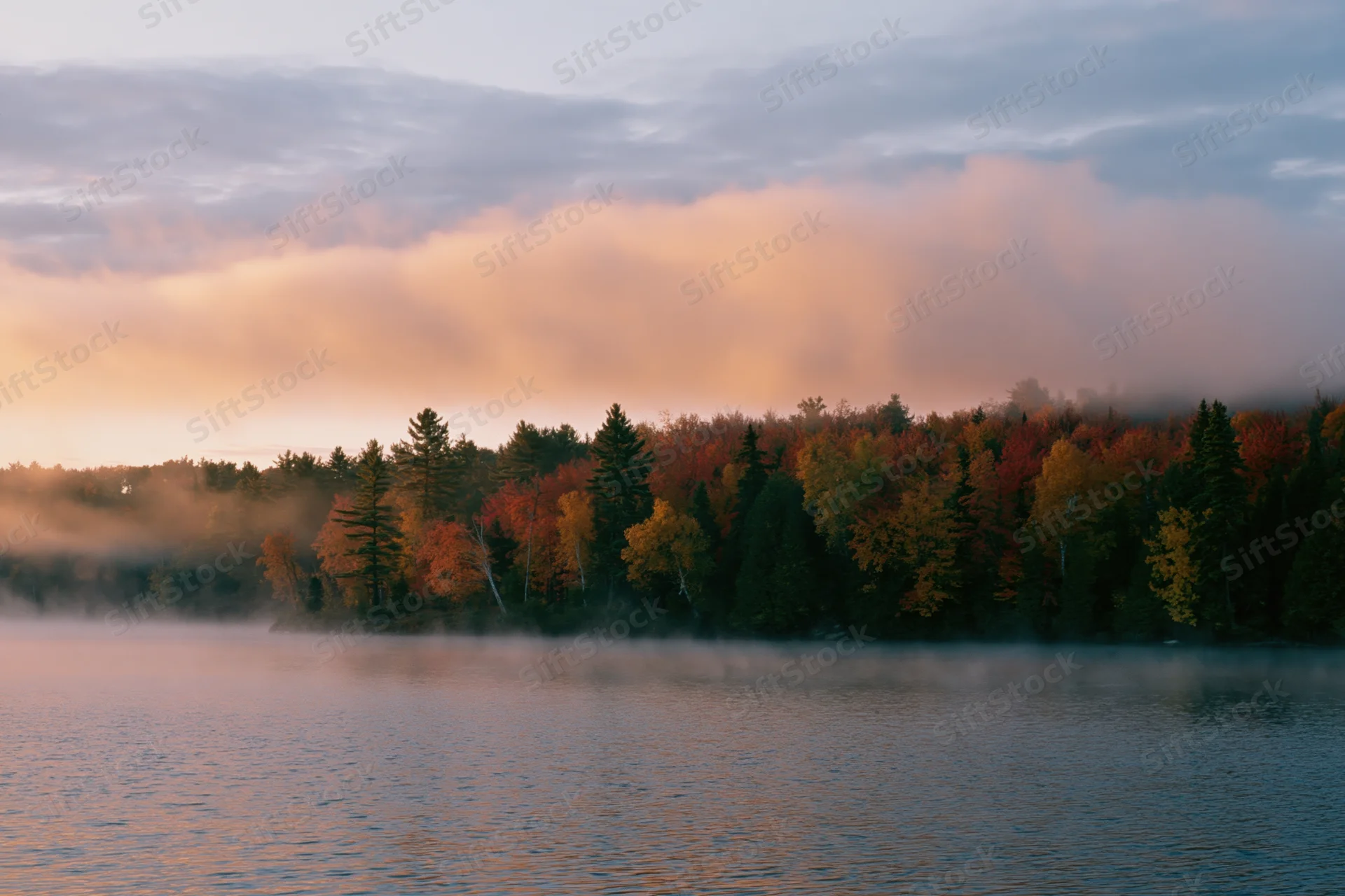 Calm lake shoreline with autumn foliage and thin morning mist reflecting in the water