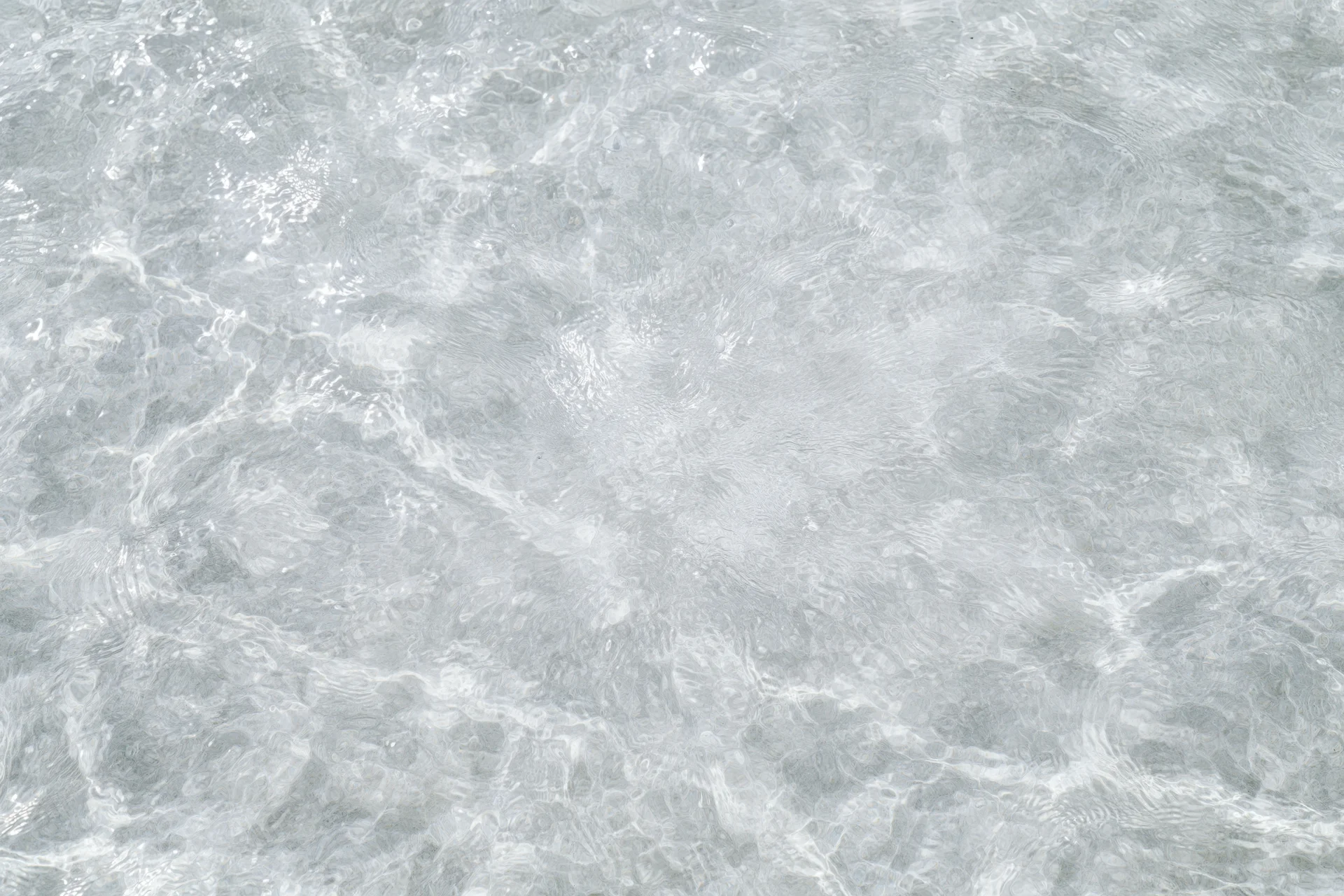 Clear shallow water surface with small ripples and light reflections viewed from above