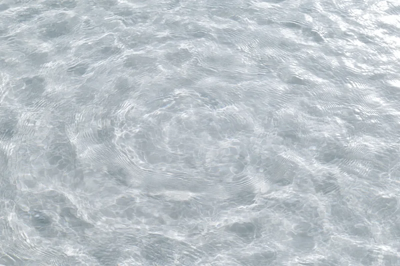 Clear shallow water surface with small ripples and light reflections viewed from above