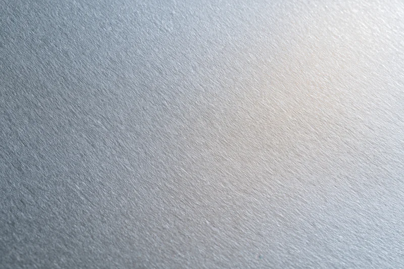 Close-up flat lay of a brushed aluminum surface with frosted texture and subtle light gradient