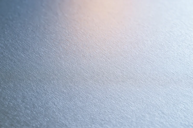 Close-up flat lay of a brushed aluminum surface with soft light gradient and visible texture