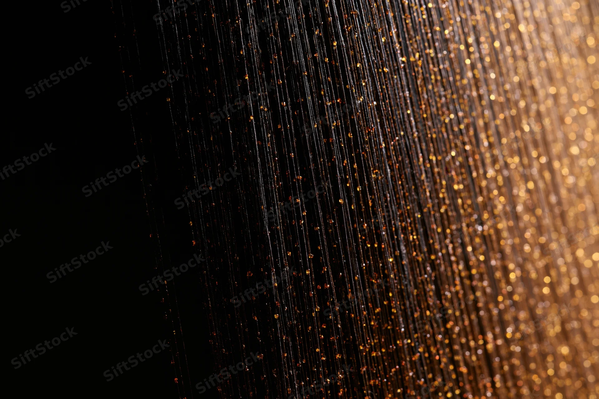 Vertical golden strands of a decorative curtain shimmering with bokeh light against dark background