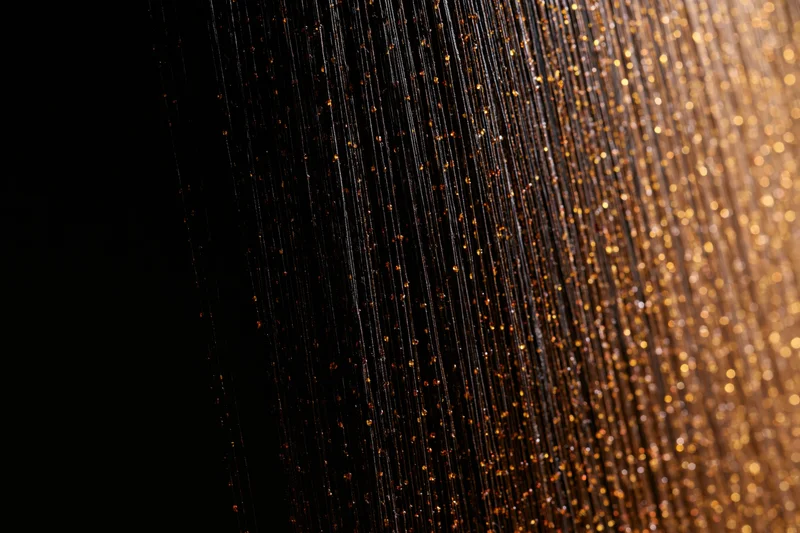 Vertical golden strands of a decorative curtain shimmering with bokeh light against dark background