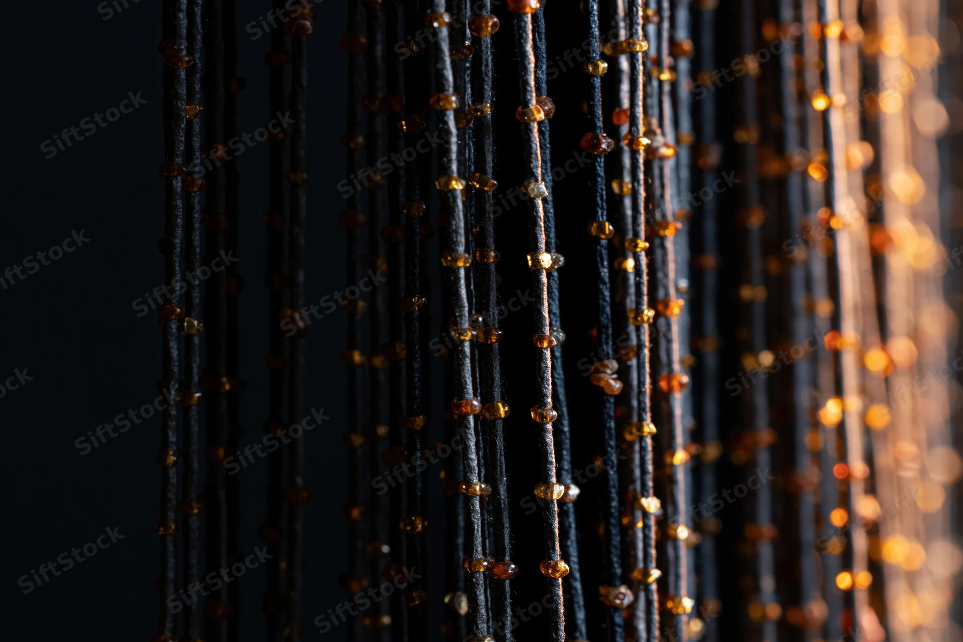 Vertical strands of black thread with amber beads hanging as a decorative curtain against dark background