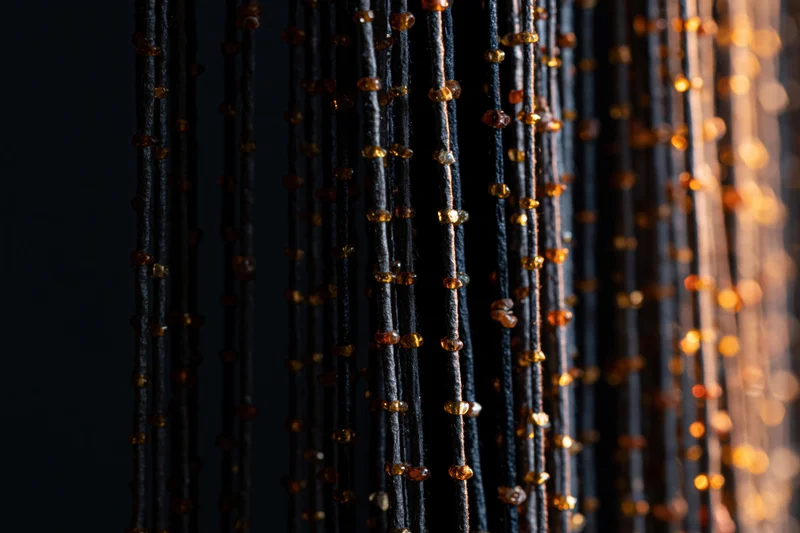 Vertical strands of black thread with amber beads hanging as a decorative curtain against dark background