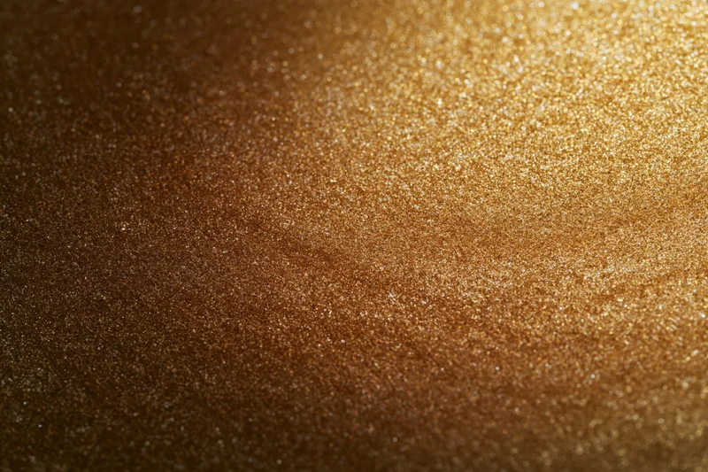 Close-up of a gold glitter-coated surface with sparkling texture and gradient lighting