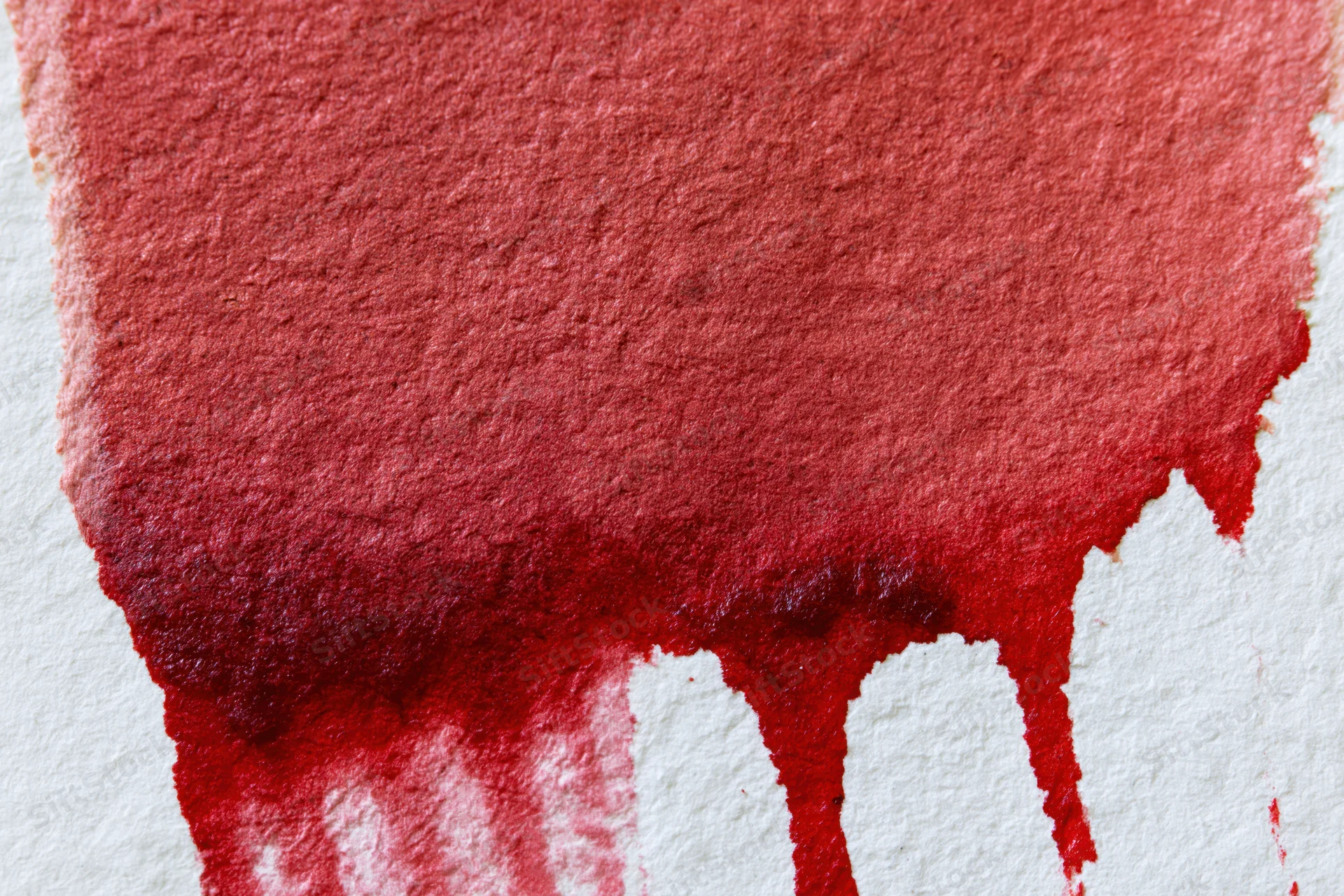 Red watercolor wash dripping on textured paper in flat lay closeup