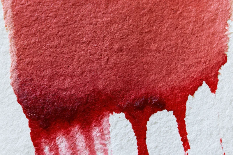 Red watercolor wash dripping on textured paper in flat lay closeup