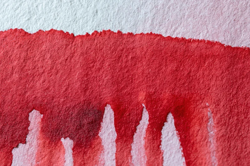 Close-up of hand-painted red watercolor wash on textured white paper with dripping edges