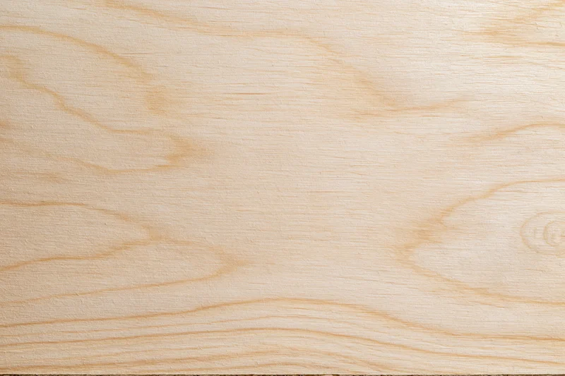 Close-up flat lay of a smooth light birch plywood surface with visible wood grain and natural texture