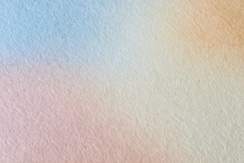 Close-up flat lay of a smooth matte paper surface with a soft pastel color gradient background