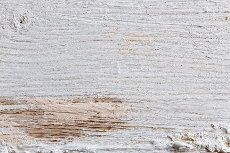 Close-up of a weathered wooden surface painted white with peeling paint and visible grain