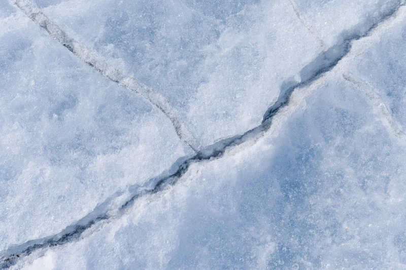 Frozen lake ice surface with diagonal cracks in winter landscape