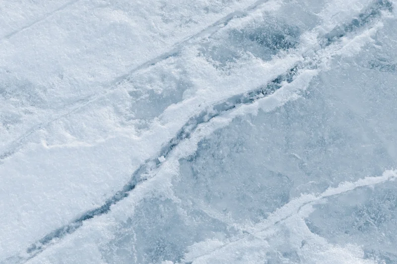 Close-up flat lay of frozen lake ice surface with diagonal cracks and frost patterns