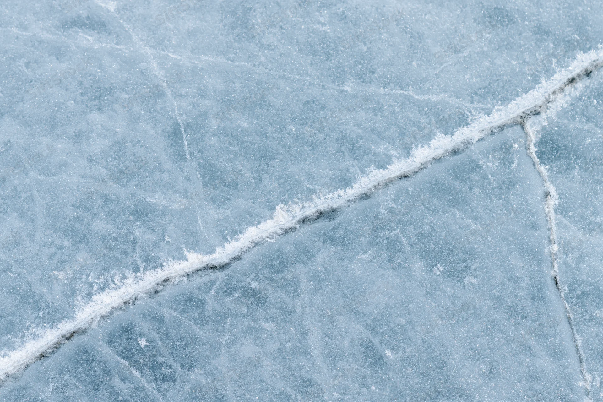 Close-up of cracked ice surface on frozen lake with frost patterns in winter