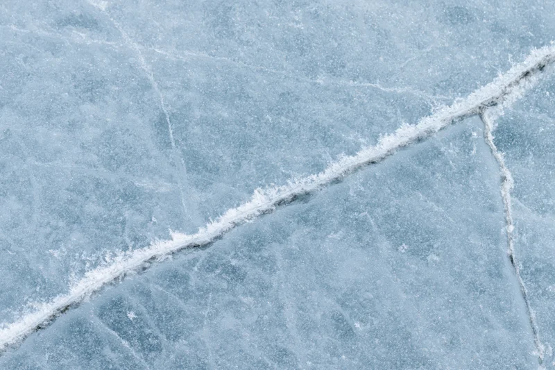 Close-up of cracked ice surface on frozen lake with frost patterns in winter