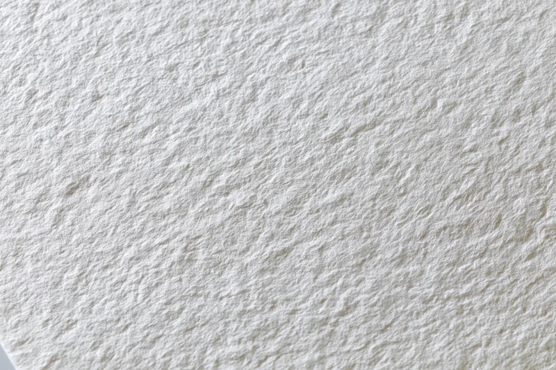 Textured white watercolor paper filling the frame in a flat lay closeup
