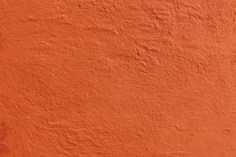 Close-up of an orange stucco plaster wall with rough texture and even lighting