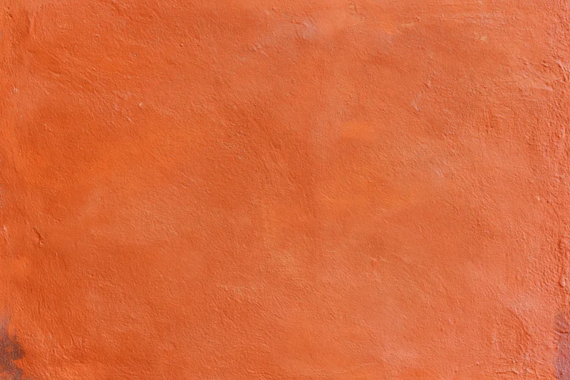 Close-up of an orange stucco plaster wall with textured surface and rough finish