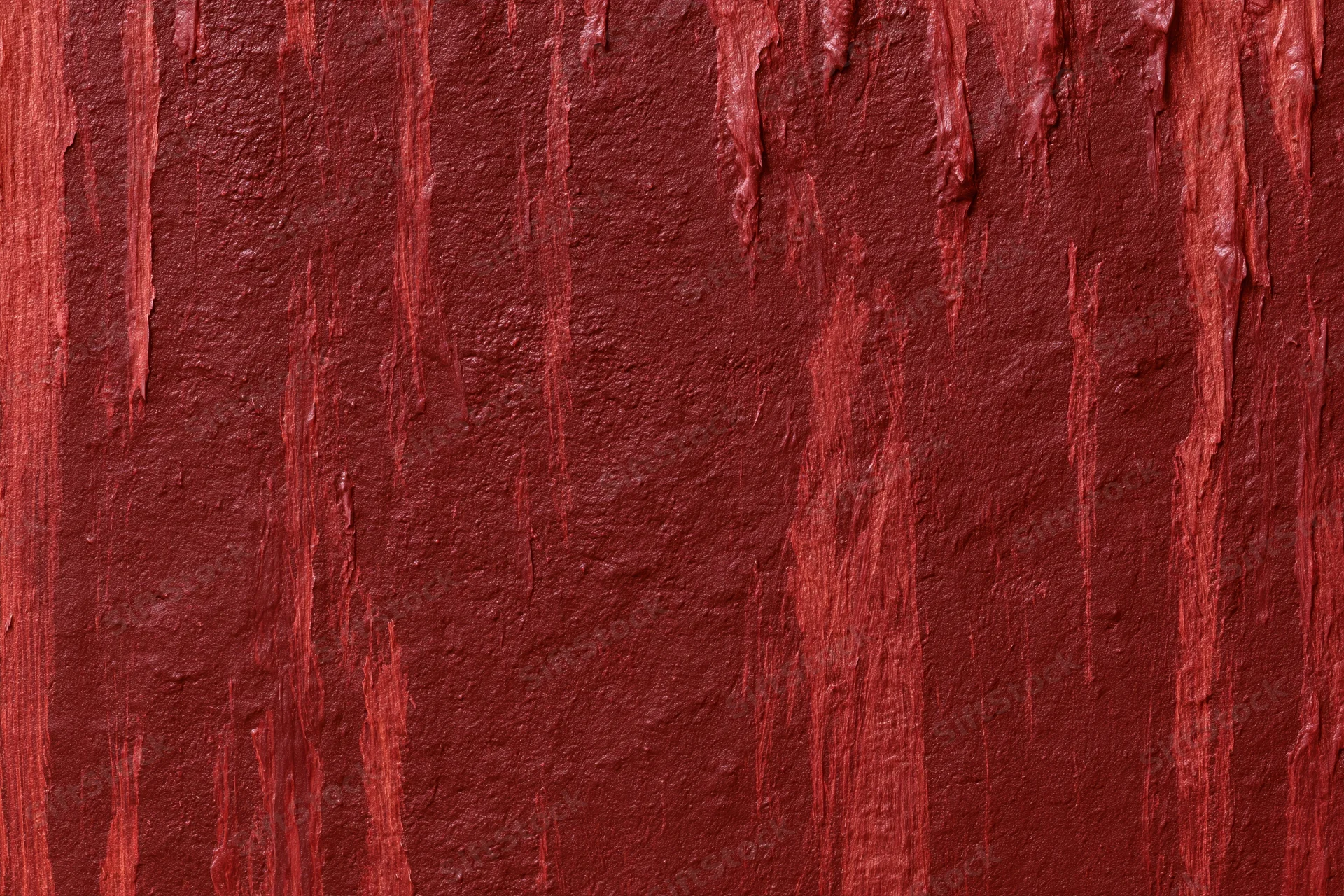 Close-up of a rough red painted wall surface with vertical drips and texture