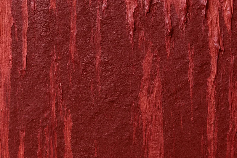 Close-up of a rough red painted wall surface with vertical drips and texture