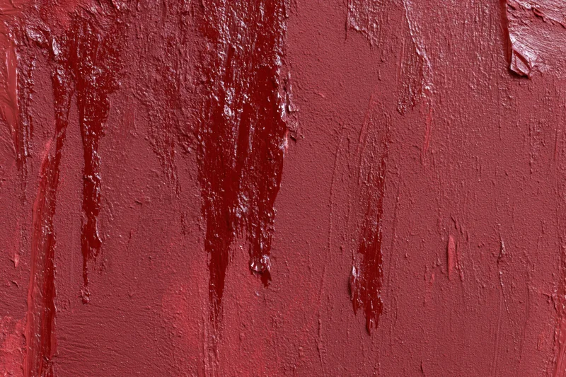 Close-up of a red painted wall with visible brushstrokes and drips showing texture and uneven coating