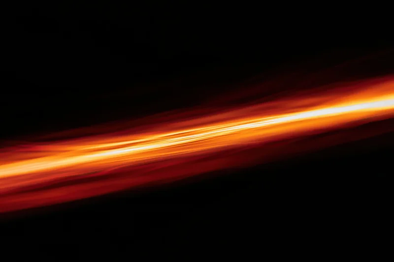 Long-exposure streak of molten light moving diagonally across dark background