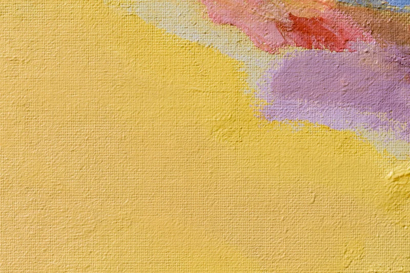 Close-up of a painted canvas surface with textured yellow and multicolored brushstrokes