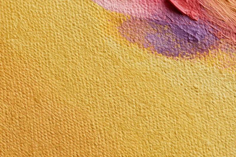 Close-up of textured canvas with yellow and red-purple paint strokes showing impasto texture