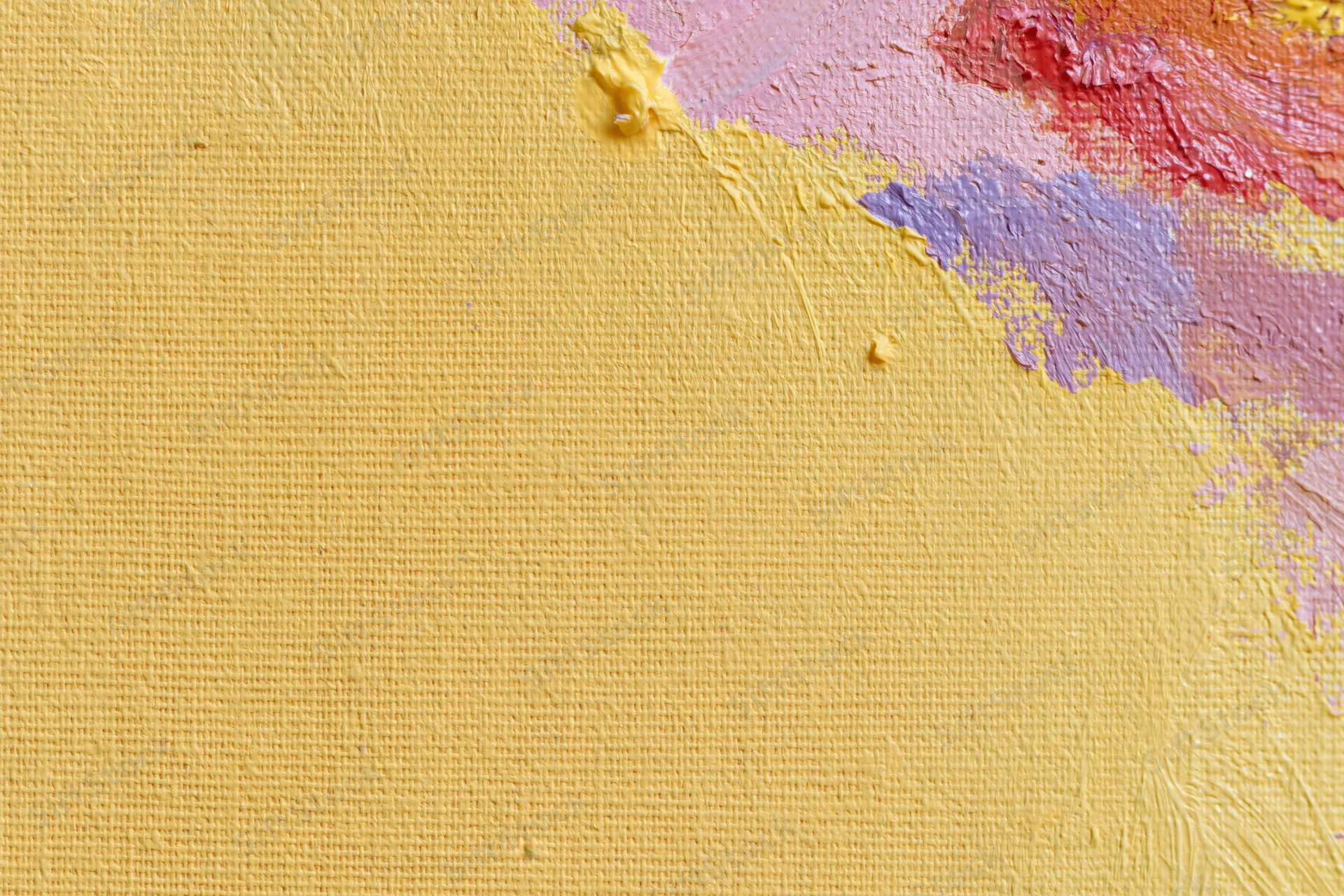 Close-up of a textured canvas surface with yellow paint and colorful brushstrokes along the edge