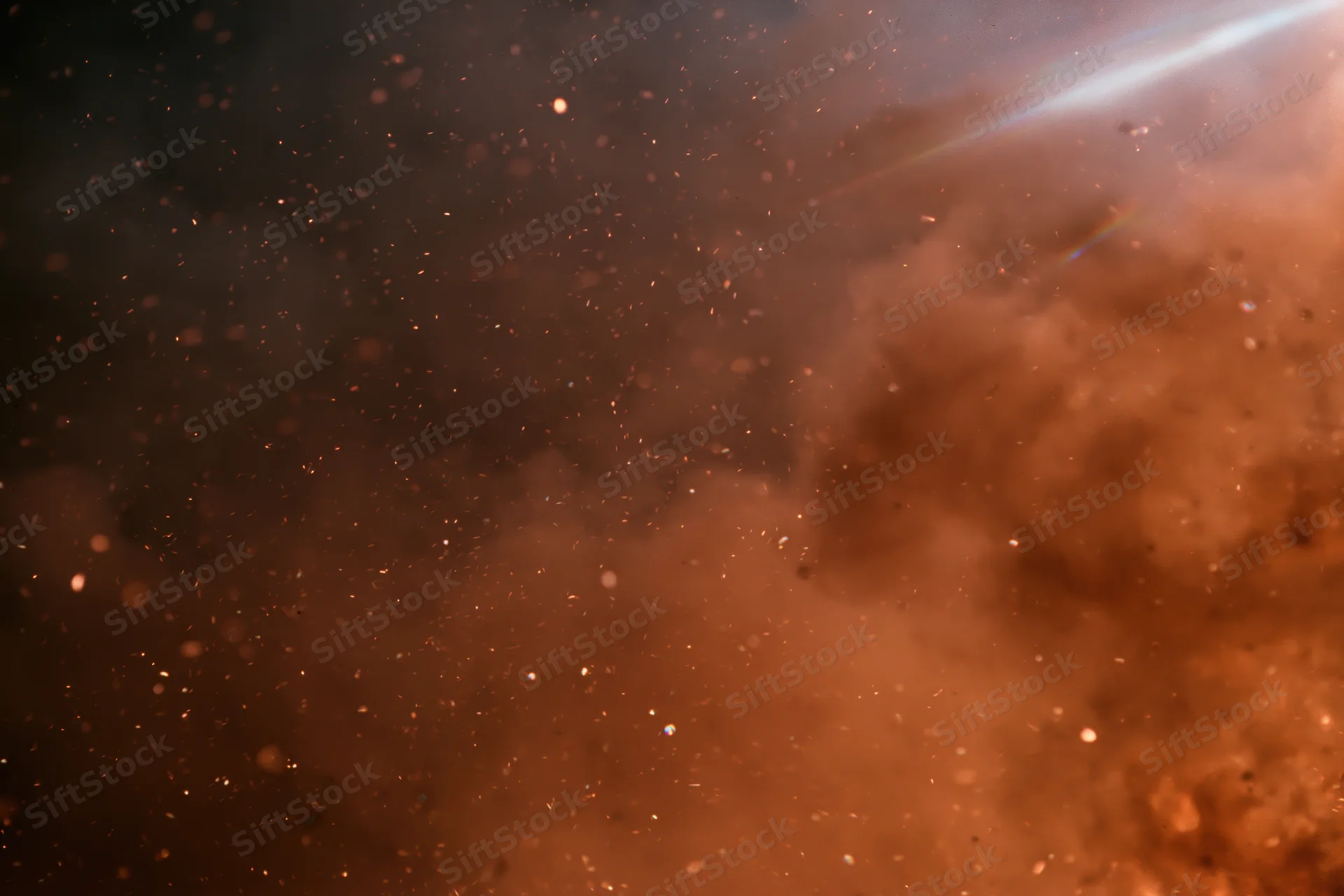 Airborne embers and sparks floating in a hazy orange-brown atmosphere with bright light streaks
