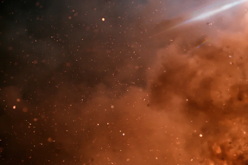 Airborne embers and sparks floating in a hazy orange-brown atmosphere with bright light streaks