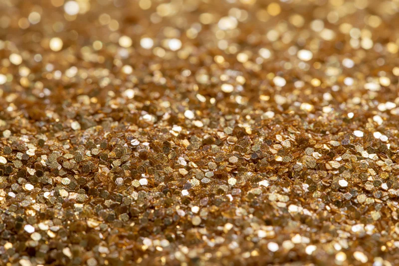 Dense gold glitter particles covering a surface in a close-up macro view
