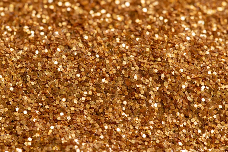 Dense gold glitter particles covering a surface in a close-up macro view