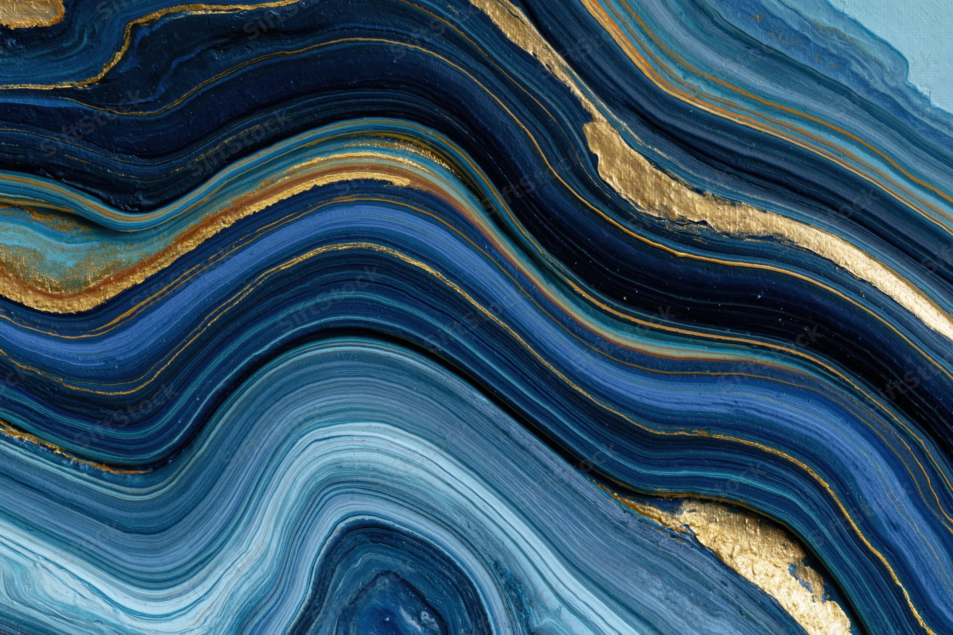 Fluid acrylic pour painting with swirling blue and gold layers on canvas