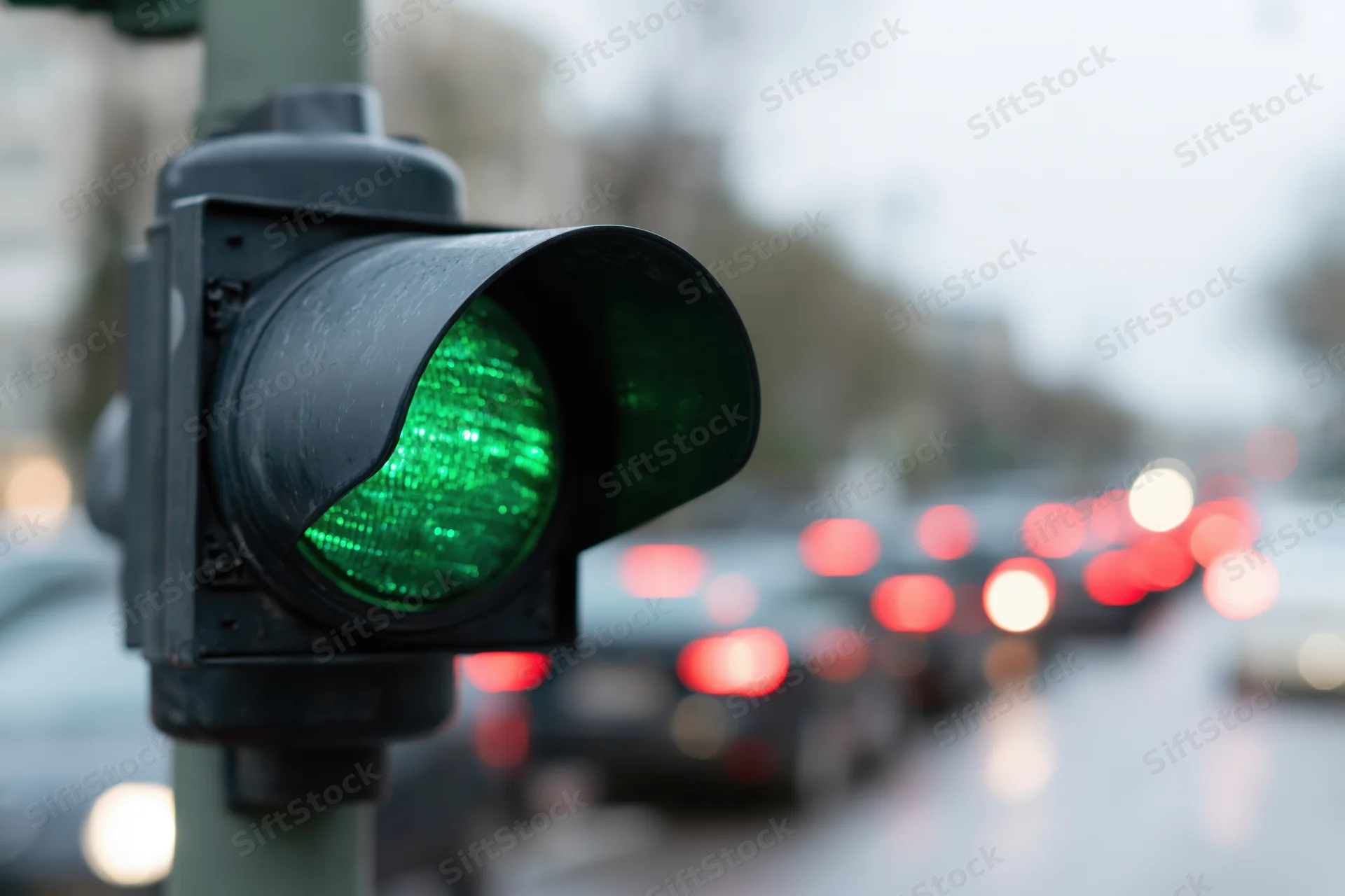 Close-up of a green traffic light signal on a city street with blurred vehicles and taillights in the background