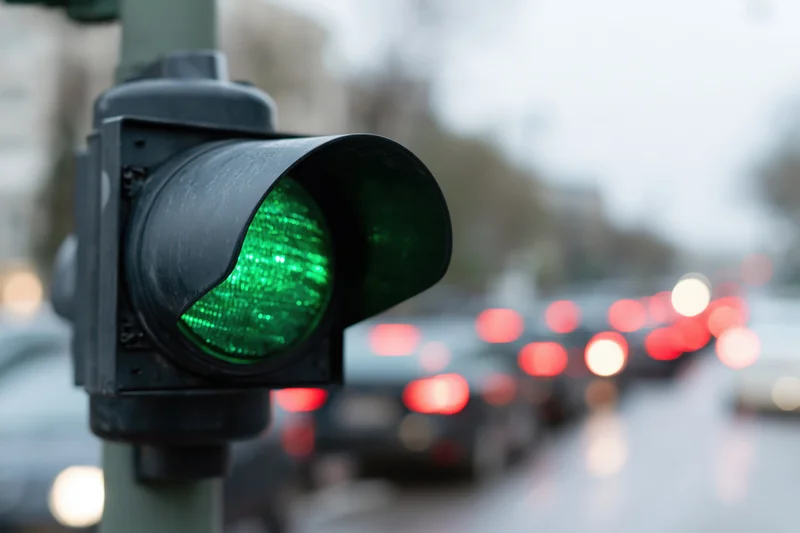 Close-up of a green traffic light signal on a city street with blurred vehicles and taillights in the background